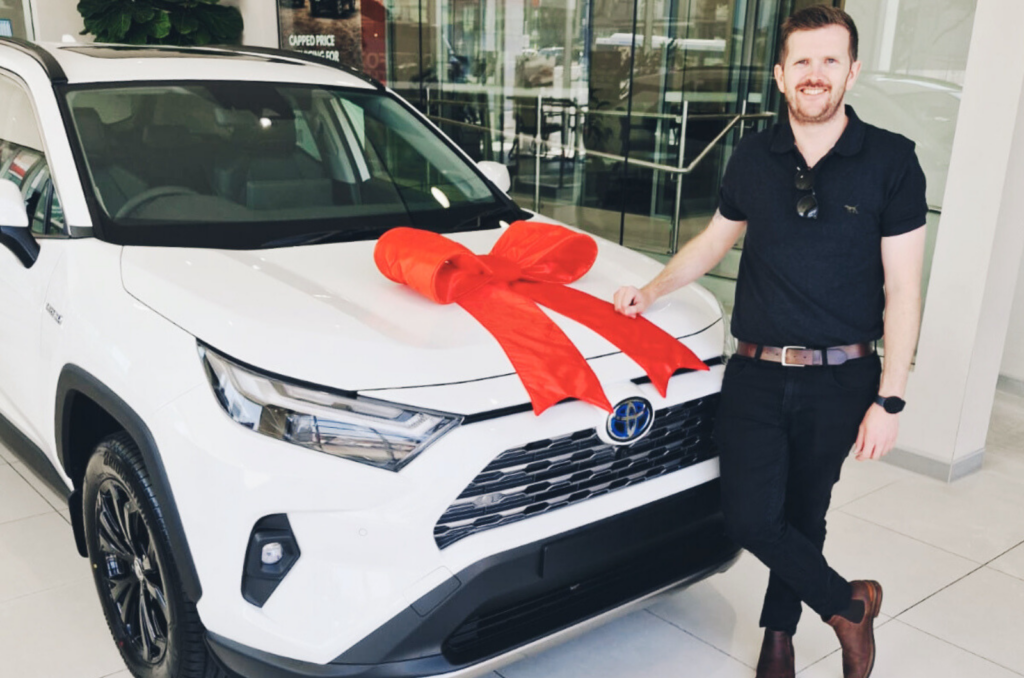 White Toyota Rav 4 Hybrid with red bow with smiling owner Red Plum Automotive car buying service